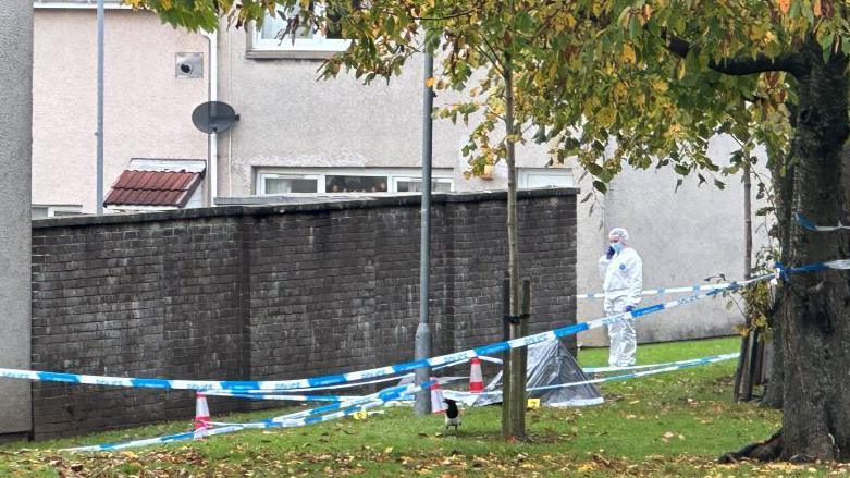 A fornesics officer in white overalls and mask near the spot where the man was found