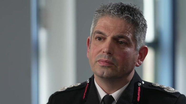 Head and shoulders of Ben Ansell looking serious. He's wearing his fire service uniform - a black blazer with red braids on the collar and silver crests on the epaulettes