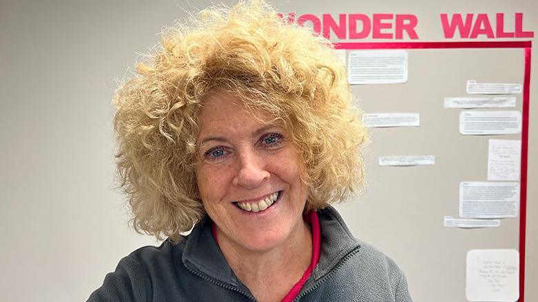 FitMums founder Sam Barlow who has curly blond hair and is wearing a grey zipped top