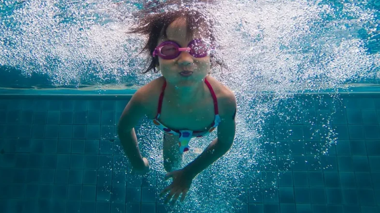 A child swims in a pool, under water and wearing googles.