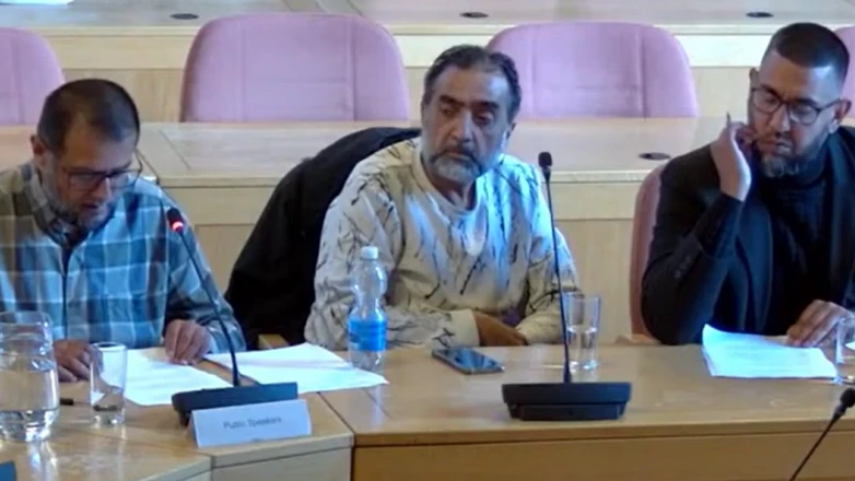 Ali wearing a blue checked shirt looking at a paper- Nawab wearing a white t-shirt with black lines and Zameer Ali in a black suit sitting in the meeting 