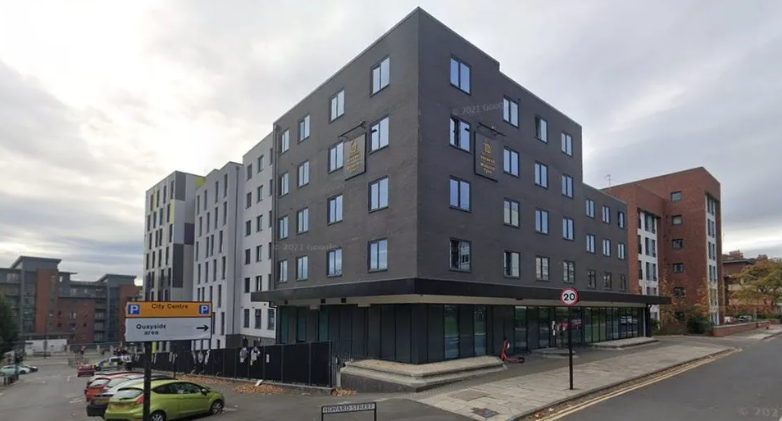 A large grey building with numerous windows and a glass-fronted entry way.