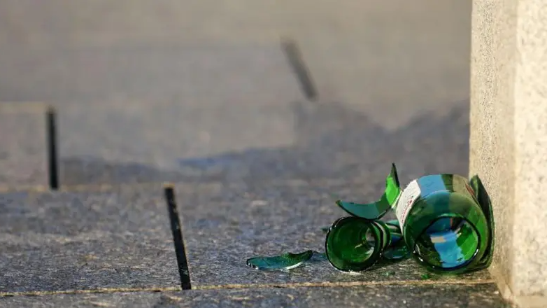 A green broken glass beer bottle left on the side of the road.