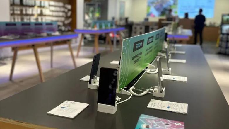 A modern shop floor of a technology/phone store, with rows of mobile phones on display.