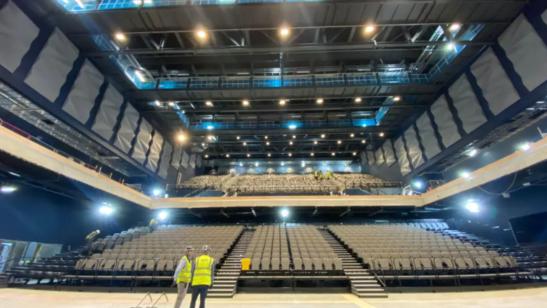 Large indoor arena with thousands of seats and stage lights 