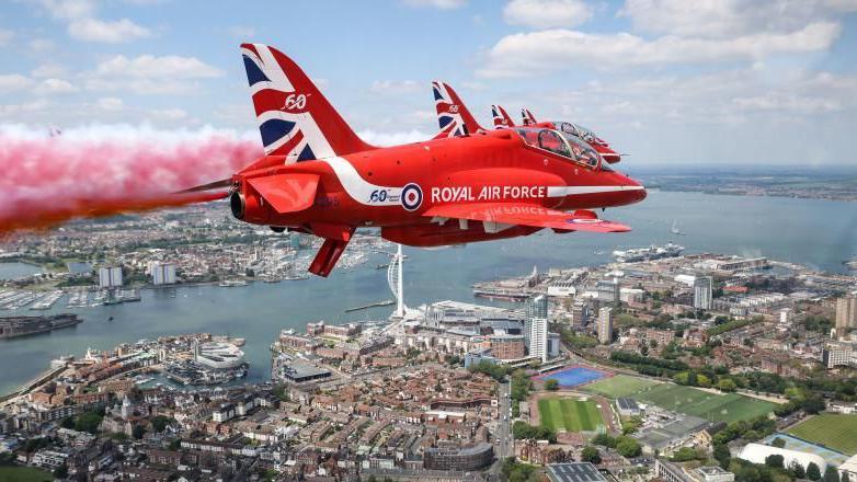 A red plane flies above houses