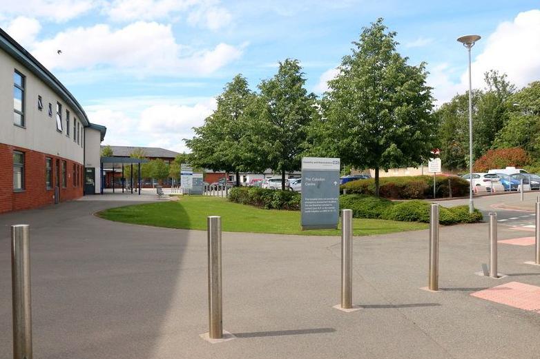 Silver bollards sit in front of a sign reading The Caludon Centre with the building and trees in the background. 