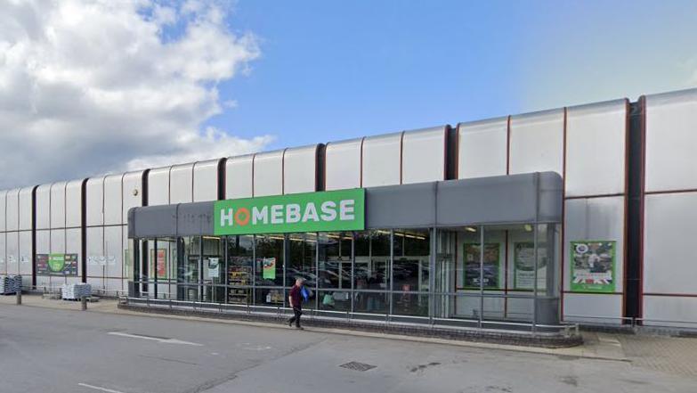 A photo of the Sainsbury's homebase store, which looks like a big silver box with rounded edges.  A green Homebase sign is stuck on the front.