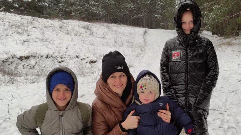 Fuzova is pictured kneeling down beside her three children in a snowy Ukraine. From left to right, the first child has a grey coat and blue hat, Fuzova is holding the second child in a navy puffer while she wears a brown coat and black hat. The third child is standing up and wears a black coat.