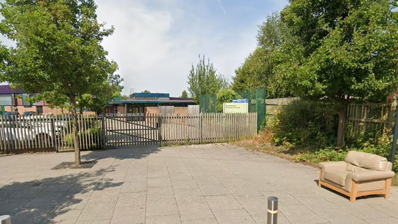 The entrance to a school campus with the word Southwark on the gate and an unexplained comfy chair on the pavement nearby