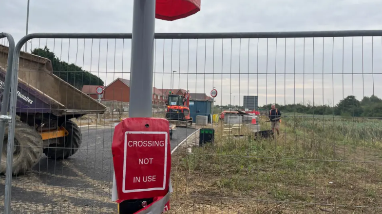 Newly installed traffic lights with fencing, construction vehicles and new housing in the background