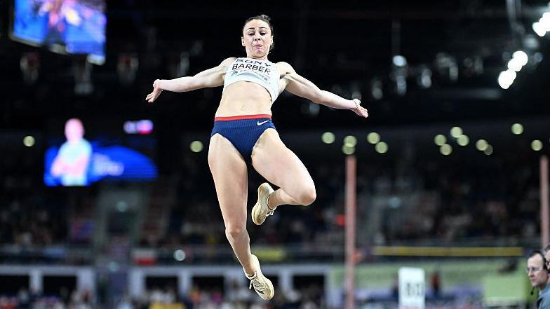 Ellen Barber, jumping in the air with her arms out wide, during the women's pentathlon long jump event at the 2026 World Athletics Indoor Championships in Torun, Poland