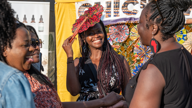 A woman holds her hat in the sunshine as she smiles in the festival sunshine