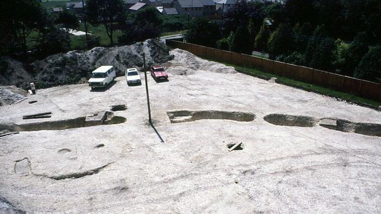 Aerial view of the original excavation. Three cars are parked on the side. It's a sunny day.