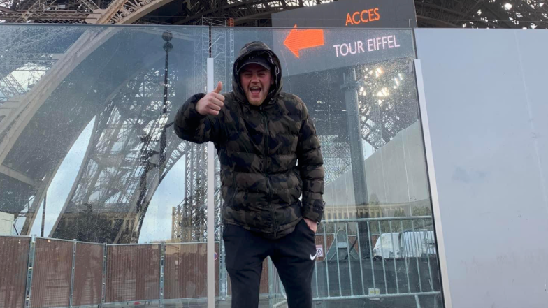 Connor Walker, with his thumbs up in front of the Eiffel Tower.