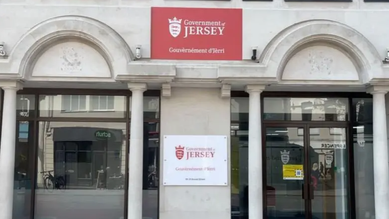 The front of the Government of Jersey building. There is a red sign at the top of the building, which says 'Government of Jersey, and two windows separated by a concrete column.