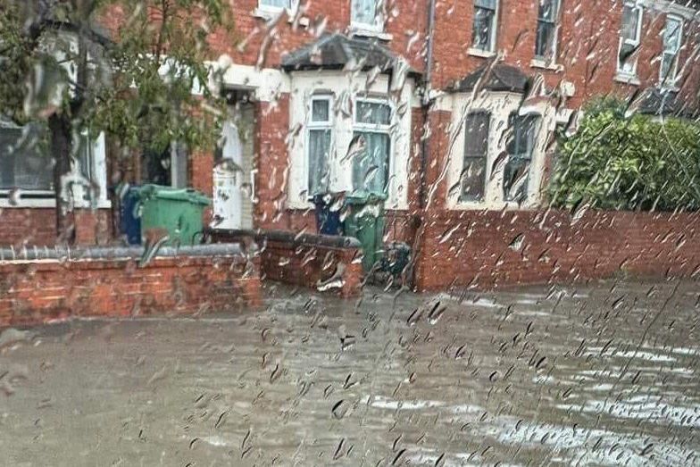 An Oxford residential road submerged underwater. The water goes right up to the front of the houses. The picture is taken through a car window, which is covered in raindrops.