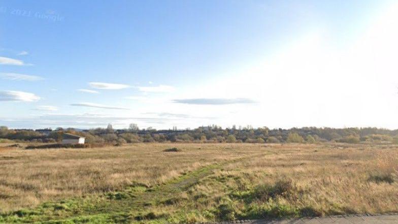 The land off Cygnet Drive. There is grass and a narrow path, with shrubs and trees in the distance.