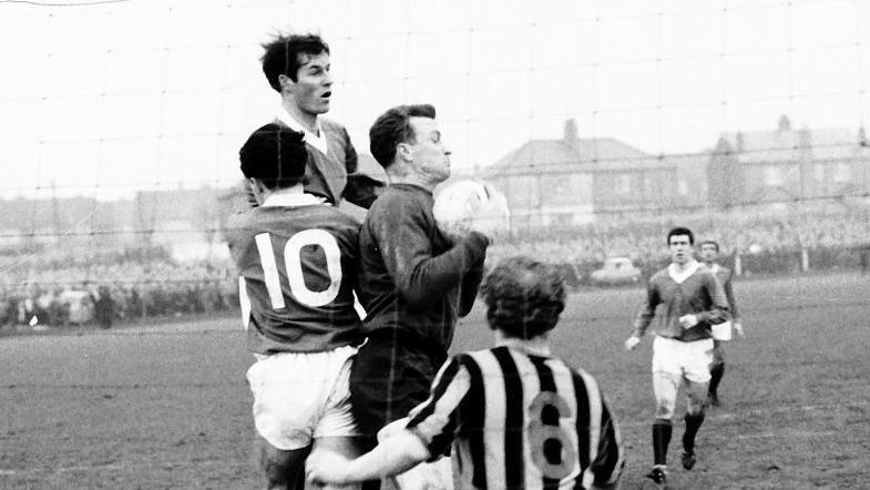 A black-and-white photograph of a football match with a goalkeeper cathing the ball