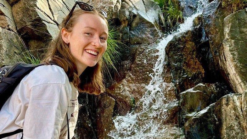Lily Sparrow, smiling at the camera, by a waterfall