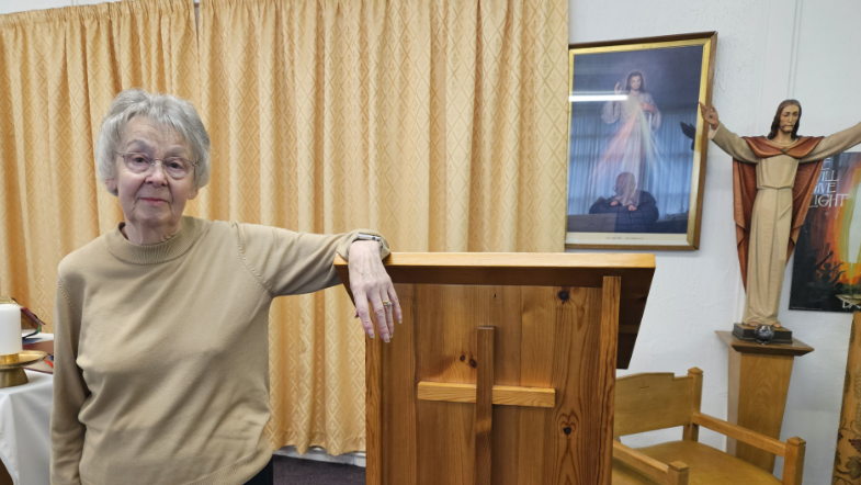 A woman in a light brown jumper and short grey hair stood by a lectern in church