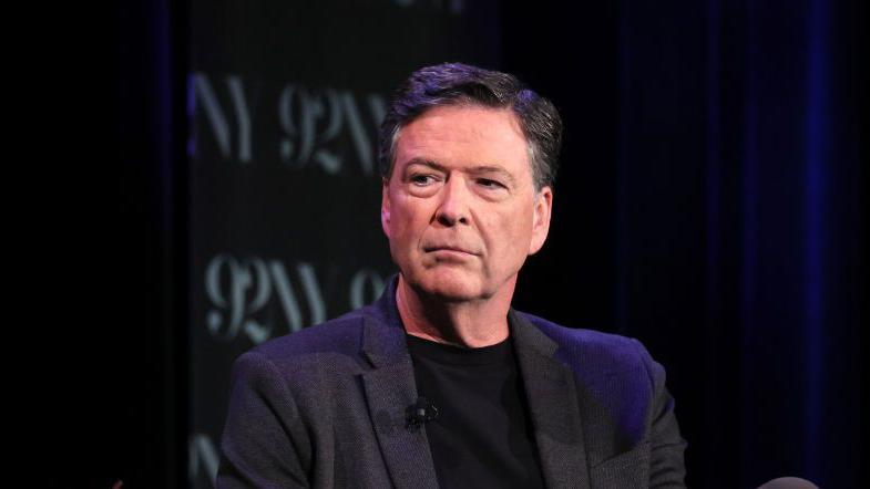 Former FBI director James Comey wearing a dark suit, with a dark background