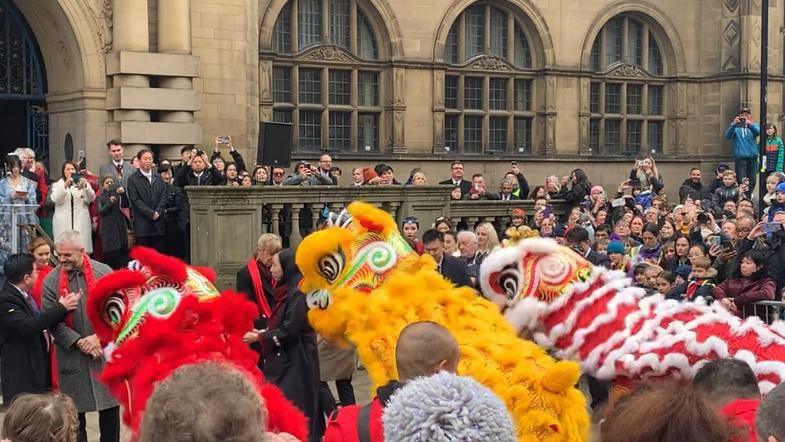 Three lion puppets in red, yellow and red and white stop in front of Sheffield Town Hall. 