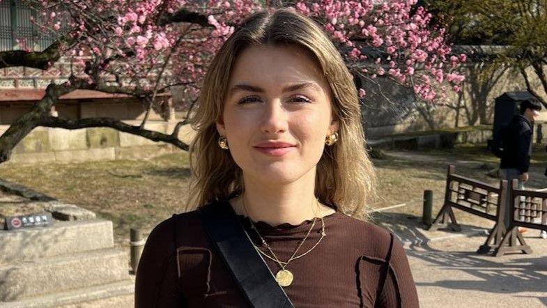 Saoirse Cleary, smiling, standing in front of a tree with pink blossom.