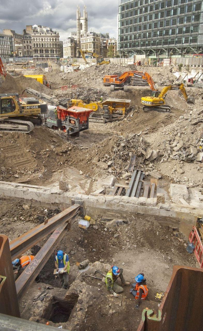 Diggers at the excavation site with modern buildings surrounding it