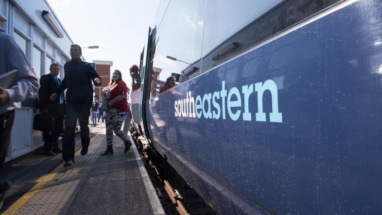 Passengers alight from a Southeastern train at a station, with the train painted in its blue and white livery.