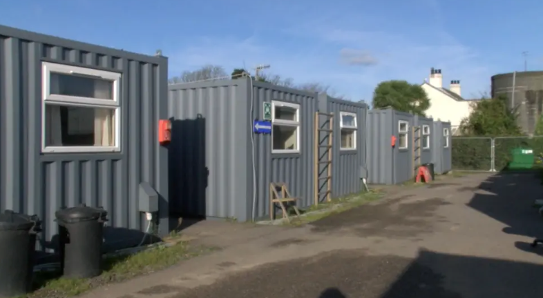 Four grey-painted corrugated iron shipping container units. 