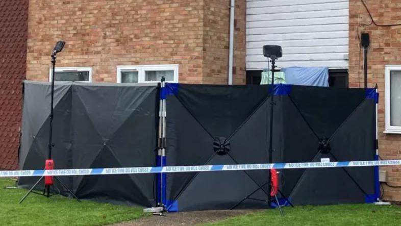 Image of a home with a police cordon going around it with a black tent covering its entrance 