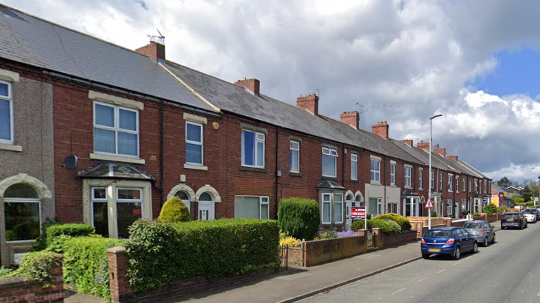 A row of red brick terraced houses on the side of a road.