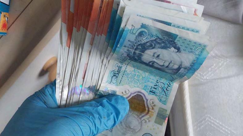 A gloved-hand holding hundreds of pounds of cash