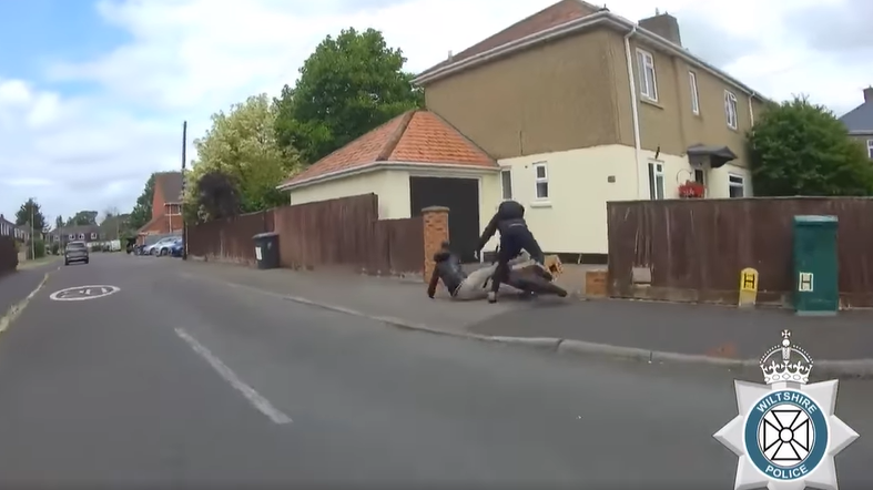 A still from a police video of two people falling to the ground from an e-bike after crashing into a wall in a residential road