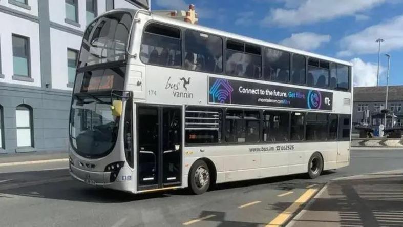 A silver double-decker bus, with a digital screen, drives away from the roundabout at the Sea Terminal.