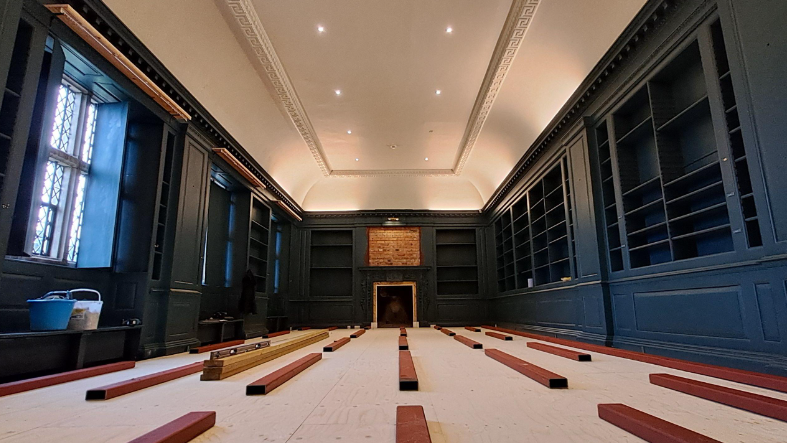 Image of Avebury Manor West Library interior with wooden planks on the floor, ready for renovation, and dark blue book cases around the edge of the room. 