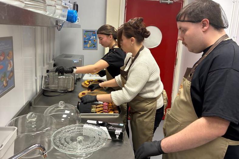 Three people in kitchen attire at a steel work bench making canapes. 