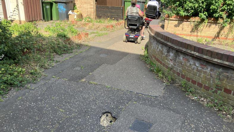 Pothole in the pavement with two mobility scooters in front it 