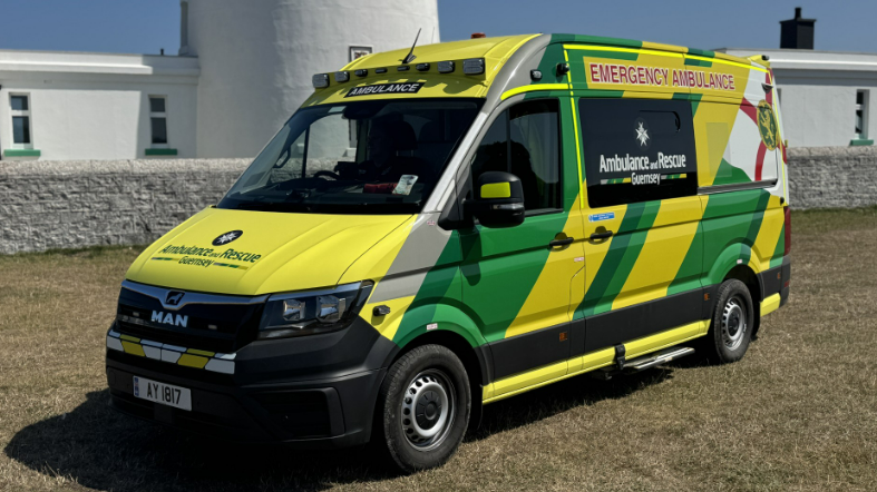 A green and yellow ambulance is parked. The Ambulance and Rescue Guernsey logo is printed on the tinted side windows.