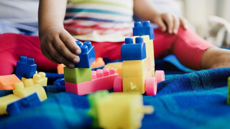 An anonymous child is sat on a blue blanket playing multi-coloured plastic toys