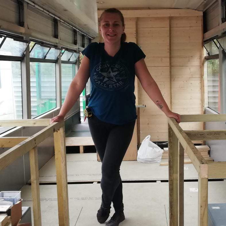 A woman leans on two wooden structures that have been built inside a bus.