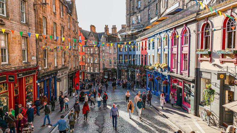 Colourful street scene in Edinburgh, with tourists walking up Victoria Street in the Old Town