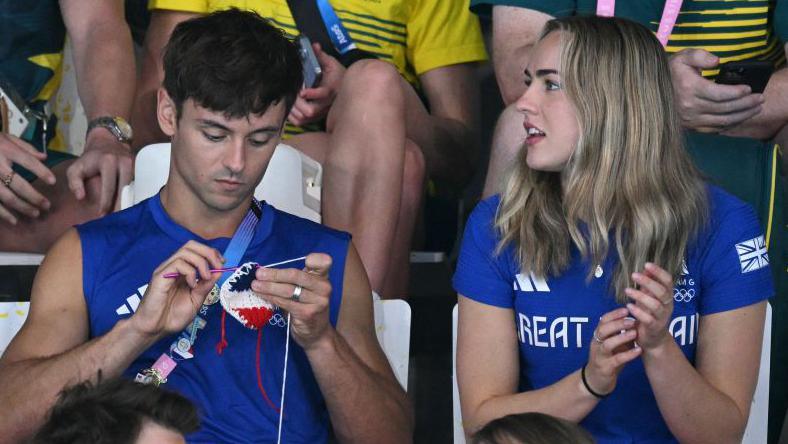 Tom Daley knitting next to Lois Toulson.