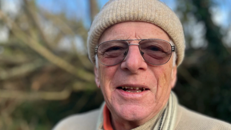 A man with a cream coloured hat and top and glasses.