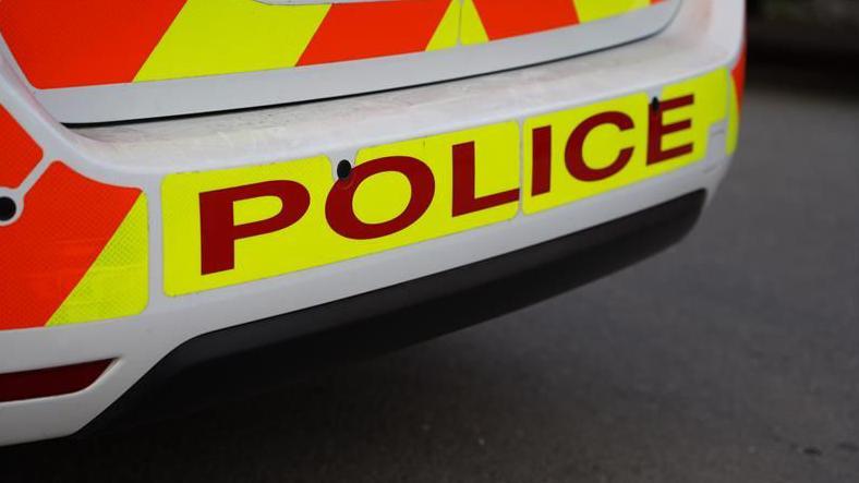An image of the rear of a police car with the sign POLICE in red lettering on an illuminous yellow background.