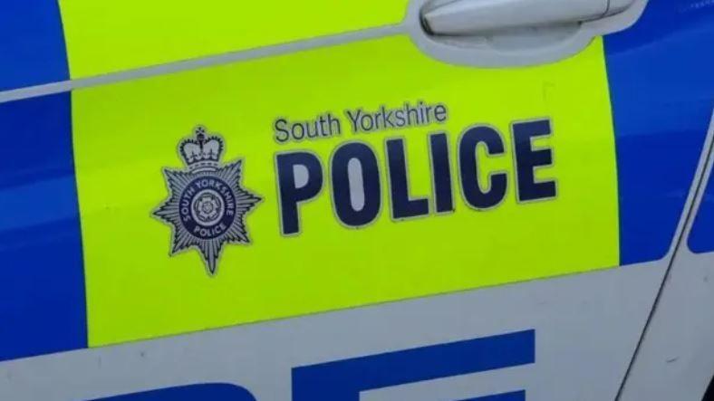 The side of a police vehicle, with blue, white and bright yellow signage. A sign on the car reads: "South Yorkshire Police."