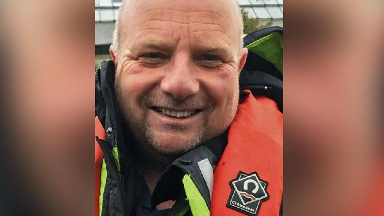 Dr Michael Roberts smiling at the camera, wearing a red coat and life jacket