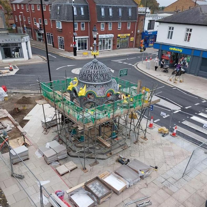 A view of the Coronation Fountain in March town centre from a third storey window. The metal structure is surrounded by scaffolding, and a mini roundabout is behind it.