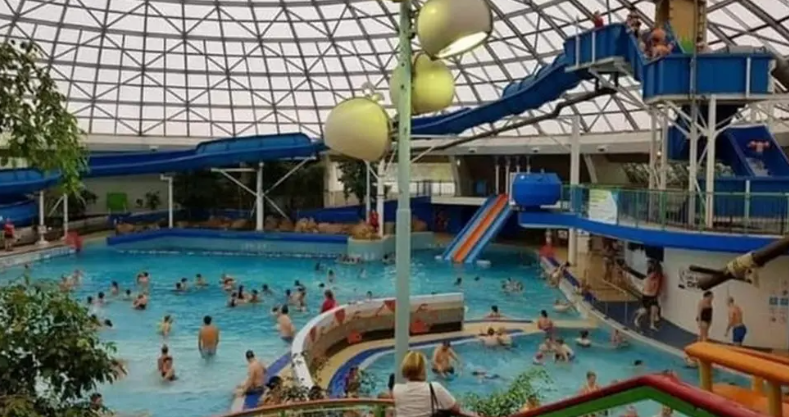 Image shows the Oasis leisure pool in action, with various slides and many people playing in the water. 